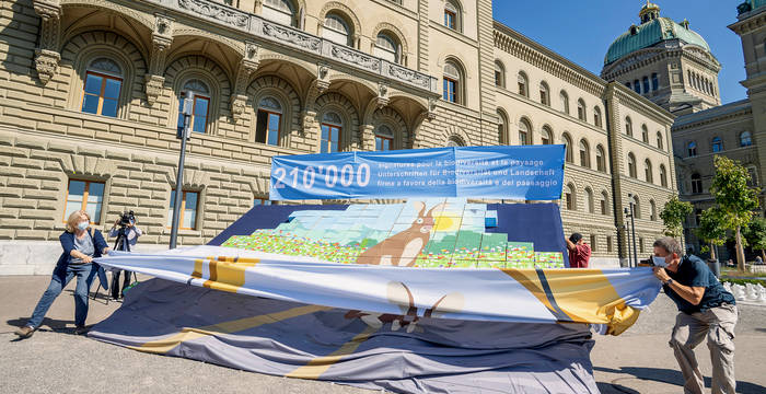 Sous le voile apparaît un puzzle de boîtes colorées: une représentation de la «Suisse de demain», riche en espèces. © Association de soutien de la double initiative biodiversité et paysage