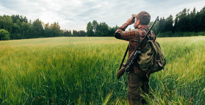 Jäger steht am Rand eines Getreidefeldes und schaut durch sein Fernglas