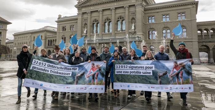 Eine Gruppe Menschen hält ein Transparent des Wasser-Appells hoch. Im Hintergrund sieht man das Bundeshaus in Bern.