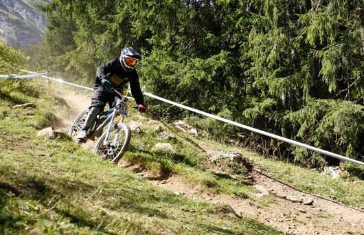 Biker auf einem kleinen Wanderweg, im Hintergrund Tannenbäume und Berge © Pro Natura, Matthias Sorg