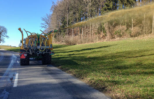 Traktor fährt auf der Strasse und spritzt Gülle