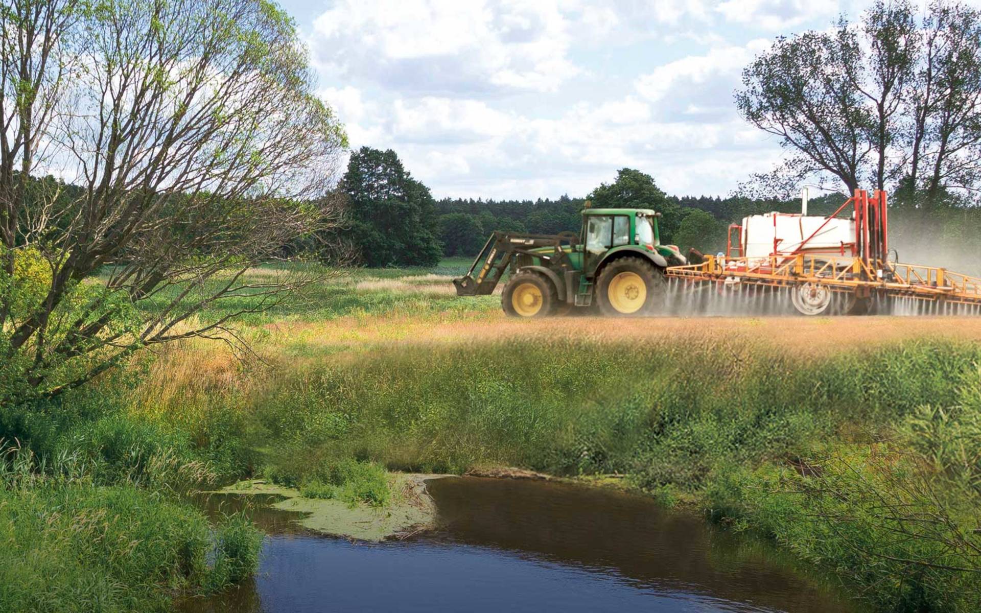 Le tracteur roule le long de la rivière au-dessus des champs et pulvérise des pesticides. © Pro Natura