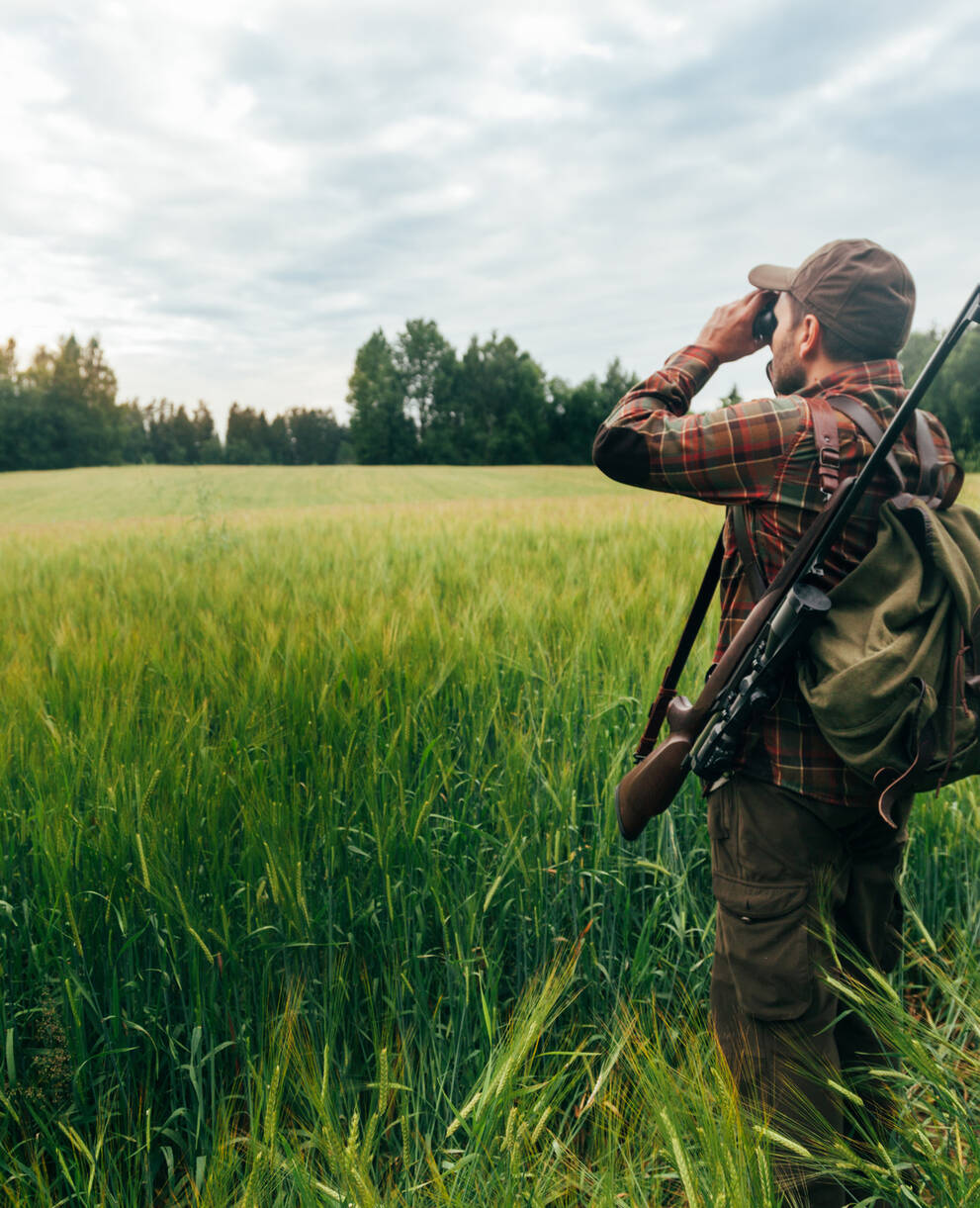 Jäger steht am Rand eines Getreidefeldes und schaut durch sein Fernglas