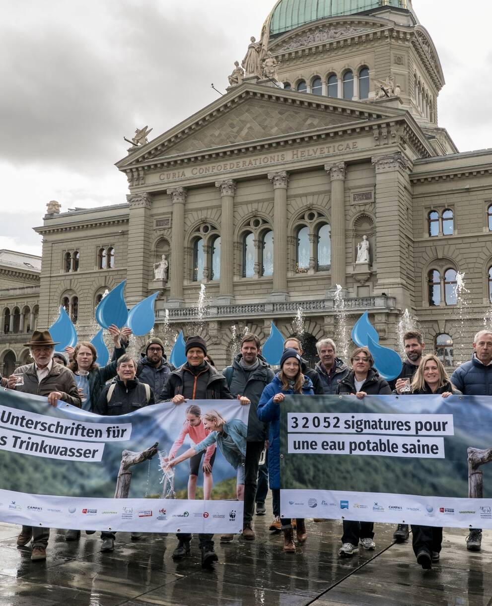 Eine Gruppe Menschen hält ein Transparent des Wasser-Appells hoch. Im Hintergrund sieht man das Bundeshaus in Bern.