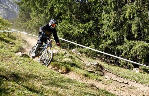 Biker auf einem kleinen Wanderweg, im Hintergrund Tannenbäume und Berge © Pro Natura, Matthias Sorg